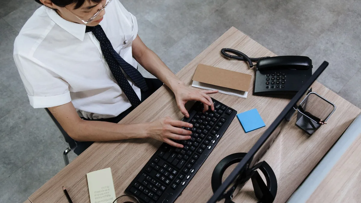 Asian man in business attire typing on a keyboard at a m