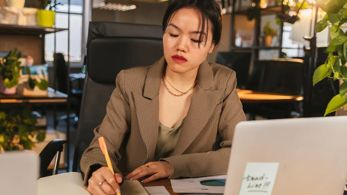 Asian woman in a business setting writing notes at a des