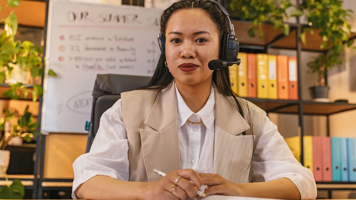 Asian woman in headset smiling while working in a modern