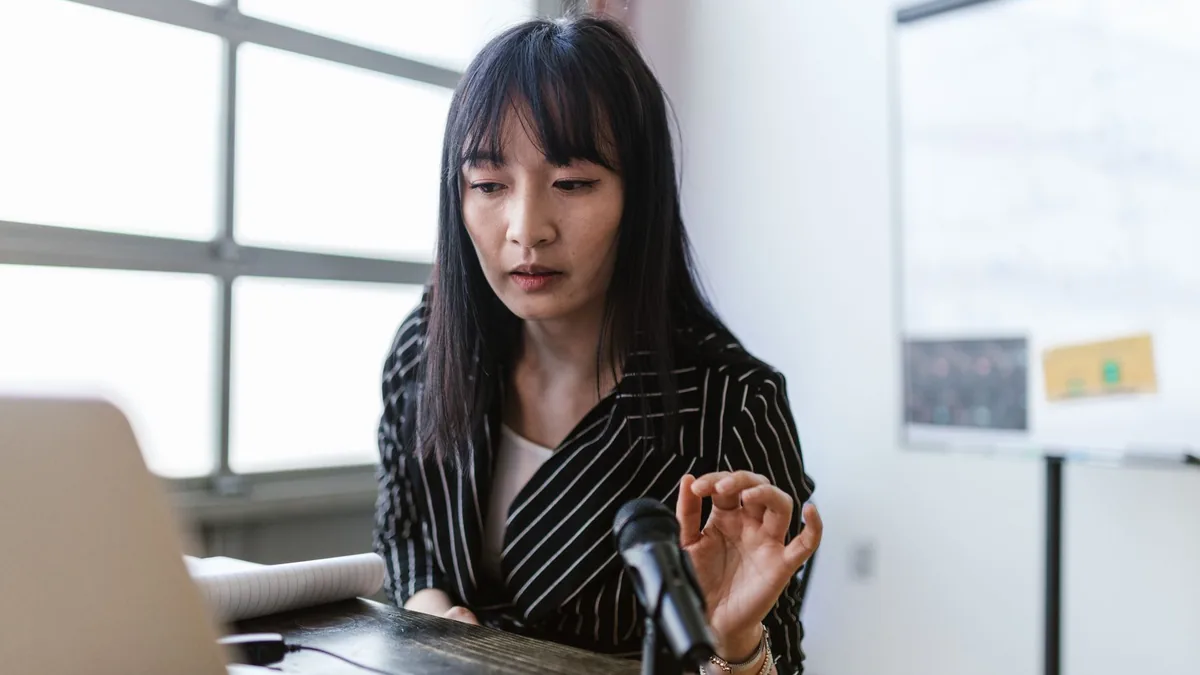 Asian woman in office presenting at a desk with a microp