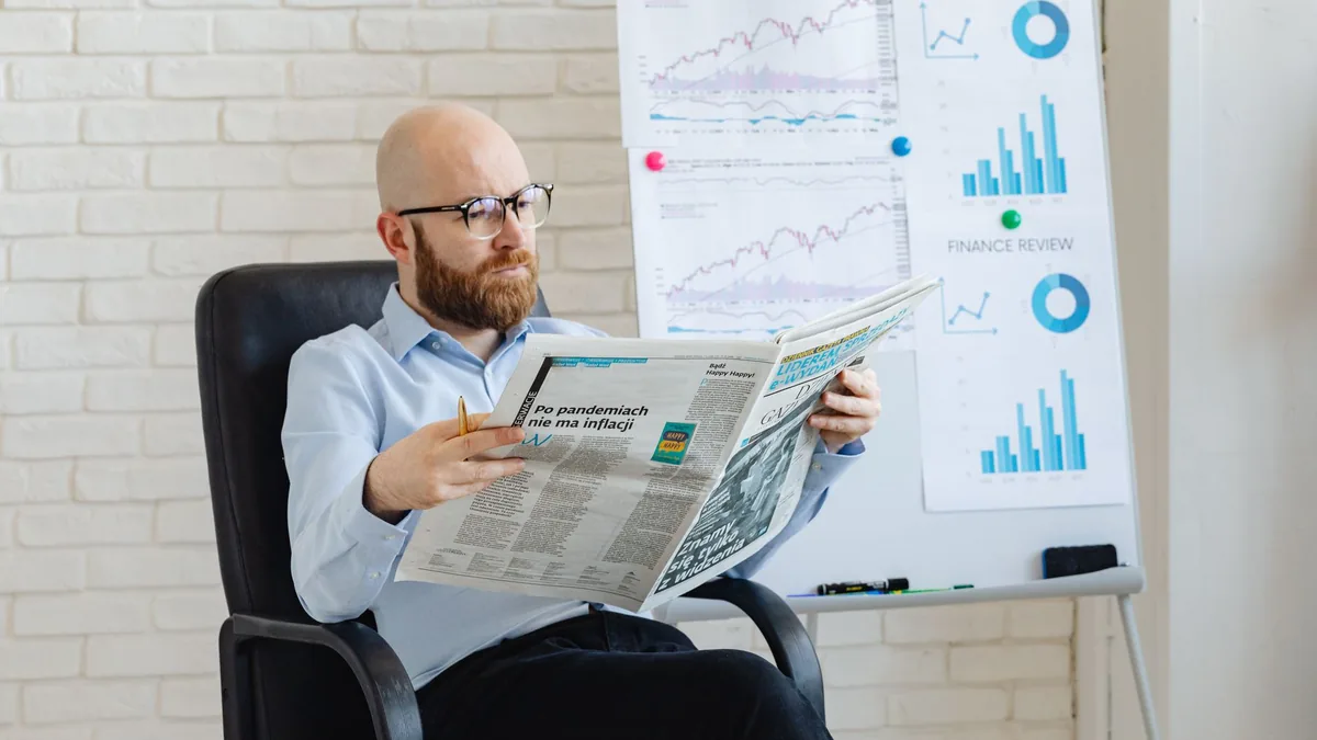 Bald man with beard reading newspaper in office with fin