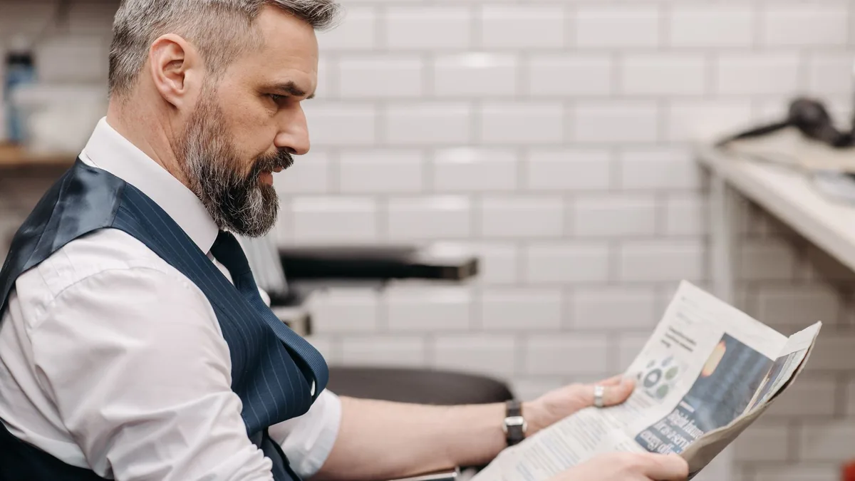 Bearded man in suit reading newspaper inside a barbersho