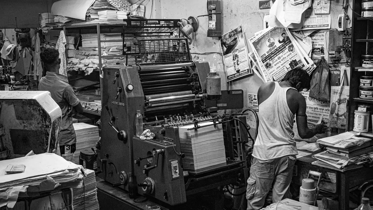 Black and white image of a bustling print shop with work