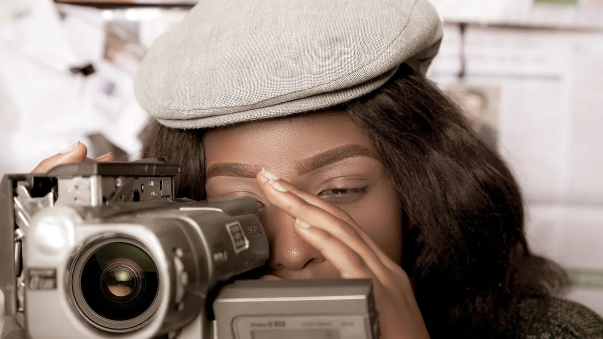 Black woman in vintage style filming with video camera e