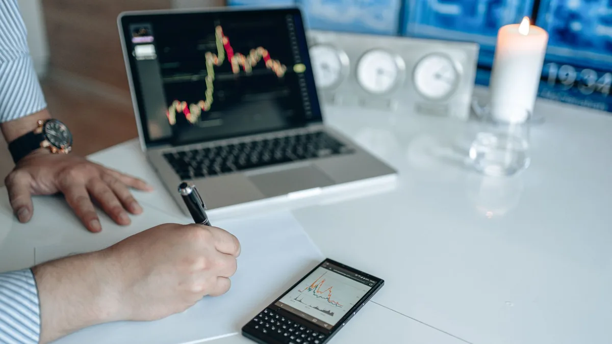 Business analyst writing with laptop and smartphone show