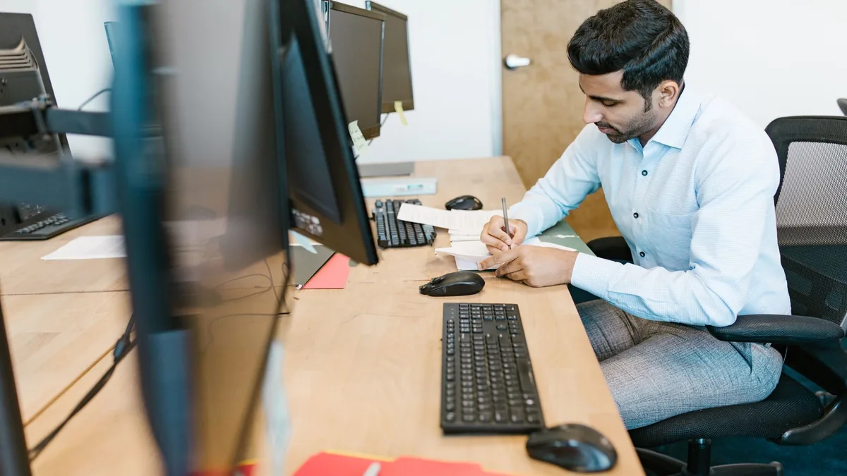 Business professional writing notes at desk with multipl