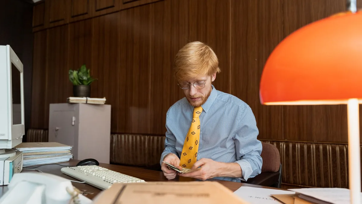 Businessman in retro office setting counting money at hi