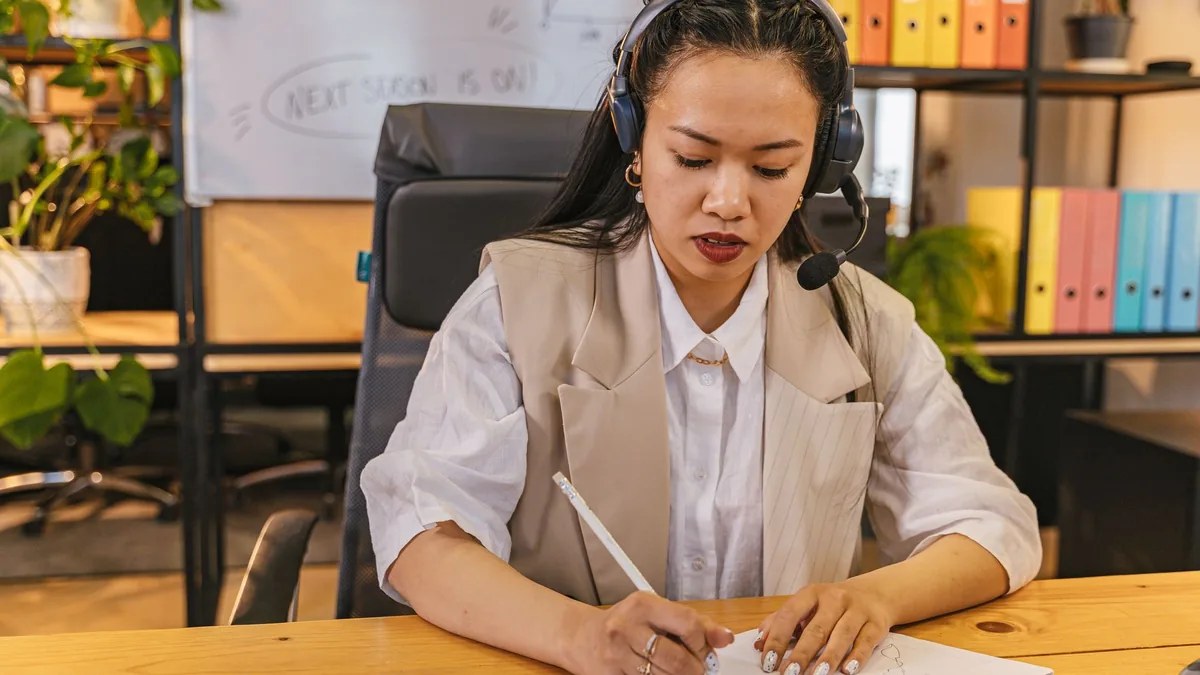 Businesswoman in headset writing notes at desk focused o