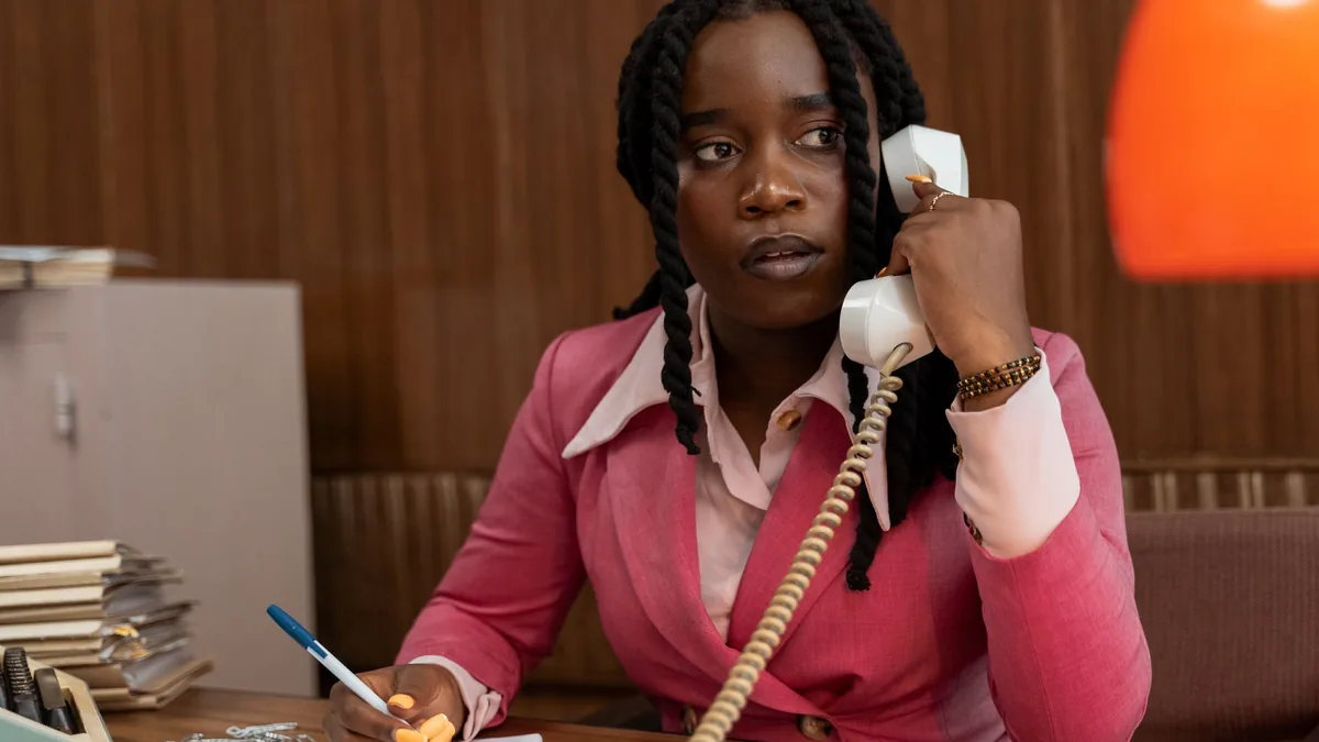 Businesswoman in pink suit talks on vintage phone at off