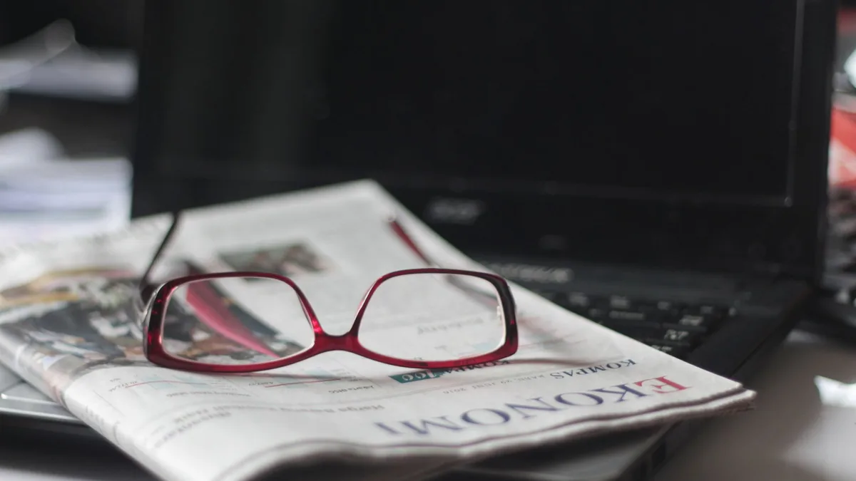 Close up of red eyeglasses on a newspaper with a laptop