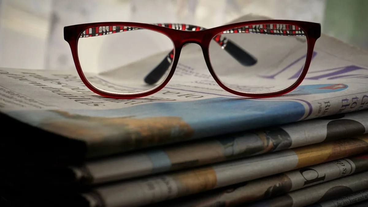 Close up of red glasses resting on stacked newspapers em