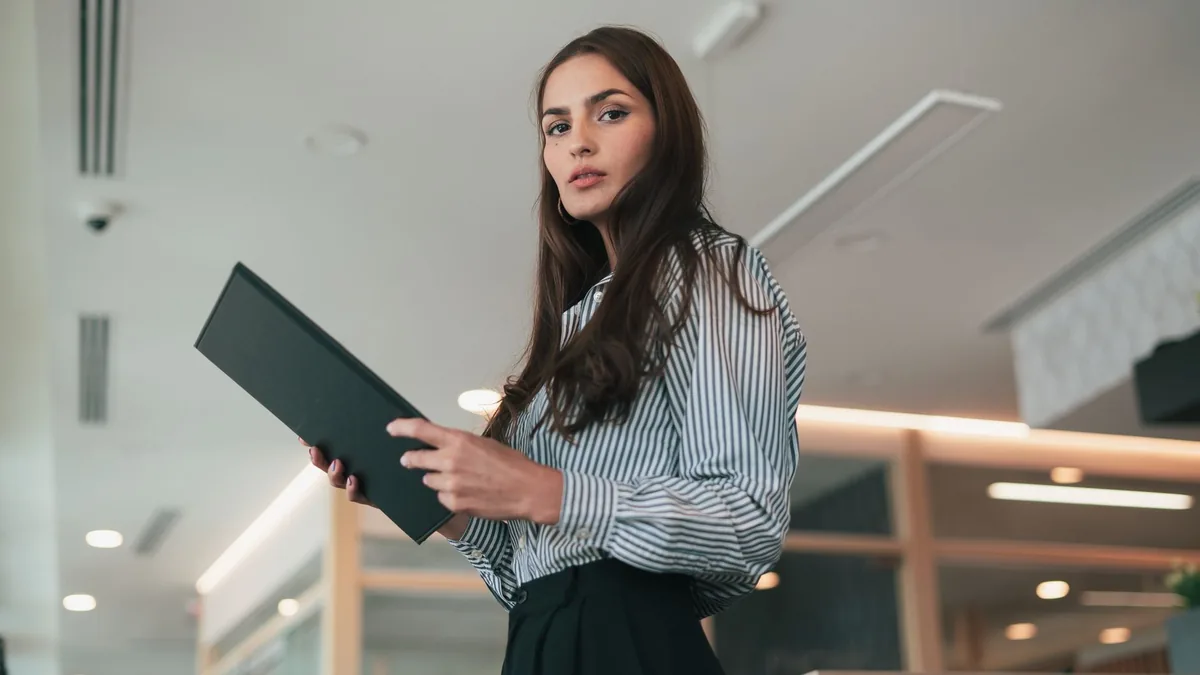 Confident woman in a striped shirt holding a black docum
