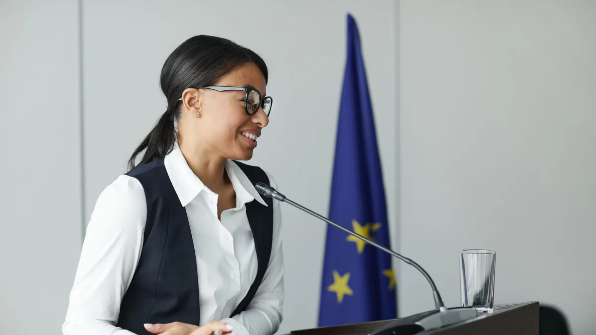 Confident woman speaker at podium with eu flag deliverin