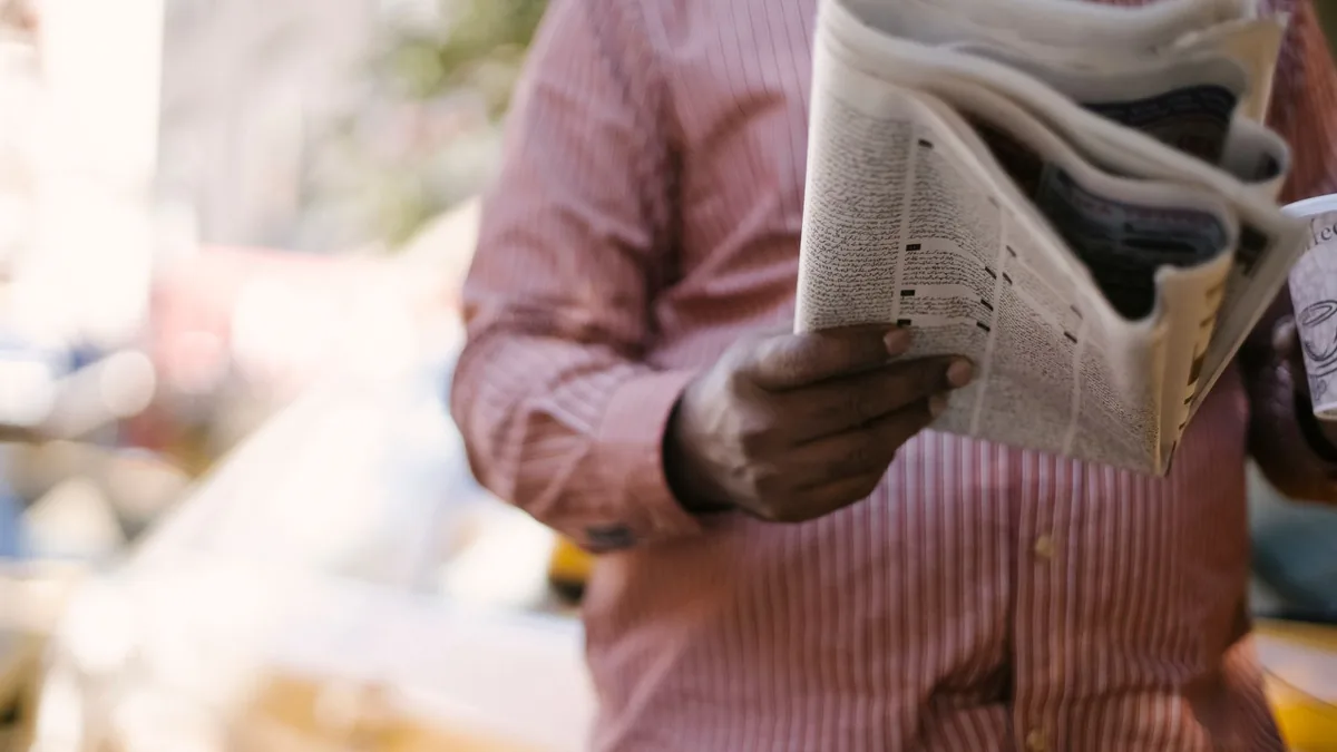 Crop unrecognizable male reading newspaper and holding p