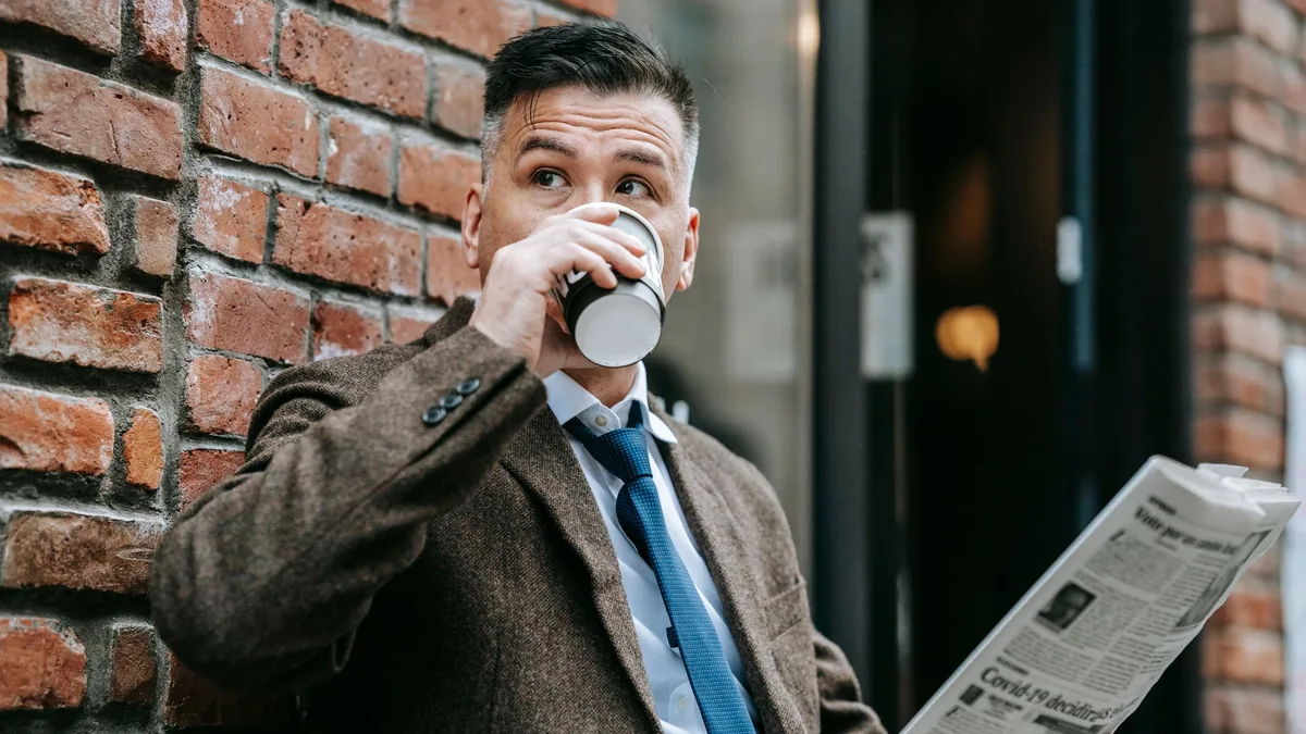 Dapper man in a formal coat drinks coffee while reading