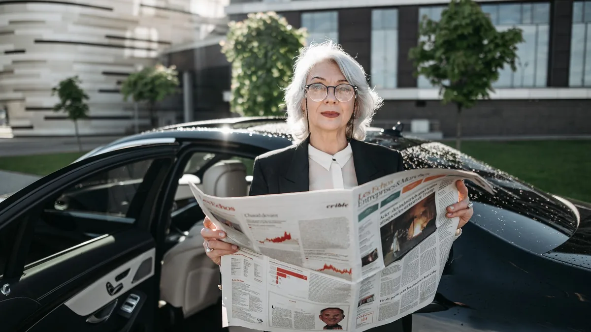 Elderly businesswoman reading a newspaper beside a car o