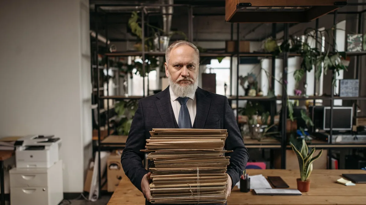 Elderly caucasian man with a beard holding piles of pape