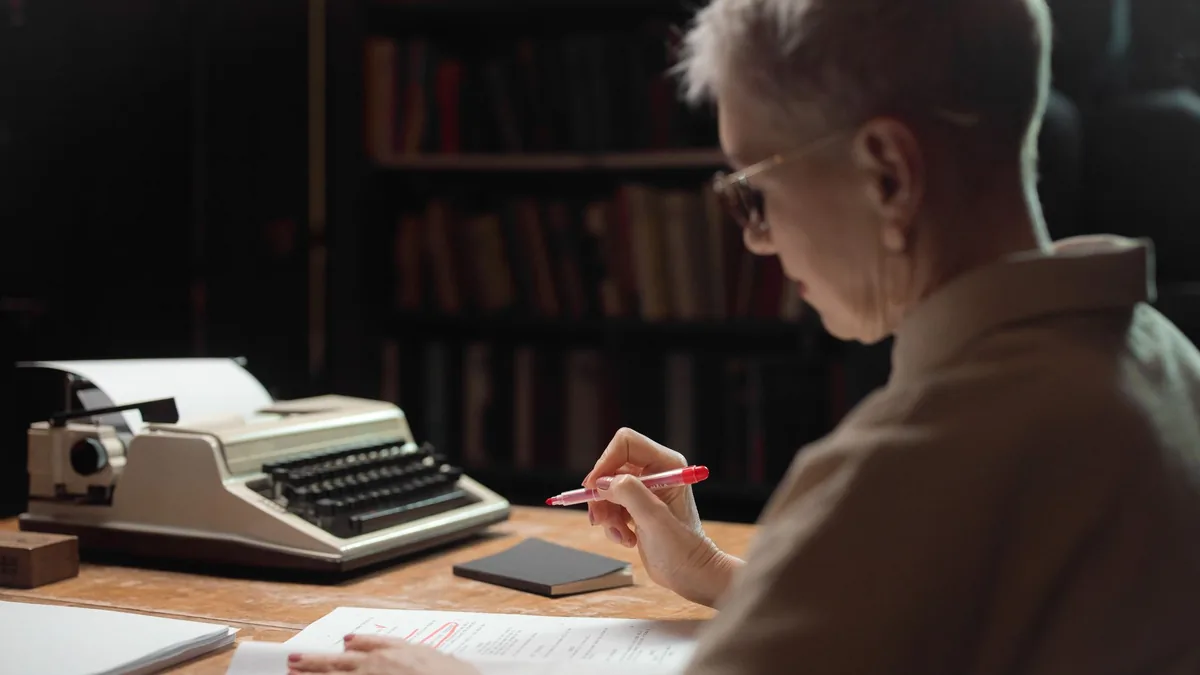 Elderly woman reviewing a manuscript with a typewriter a