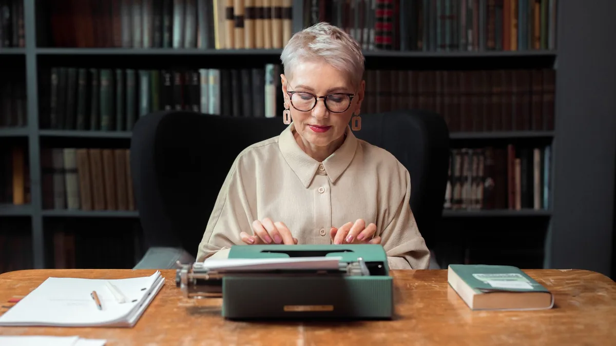 Elderly woman typing on a typewriter at a wooden table i