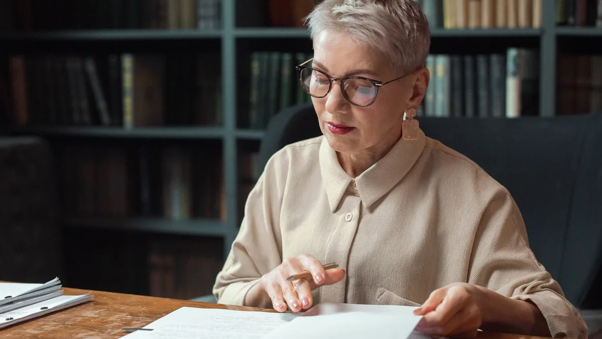 Elderly woman with glasses reading documents at a desk i