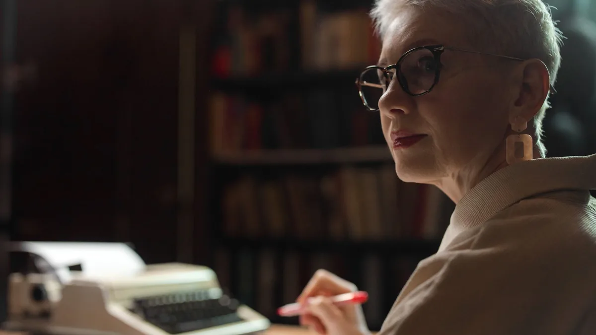 Elderly woman with glasses writing in an office with a v