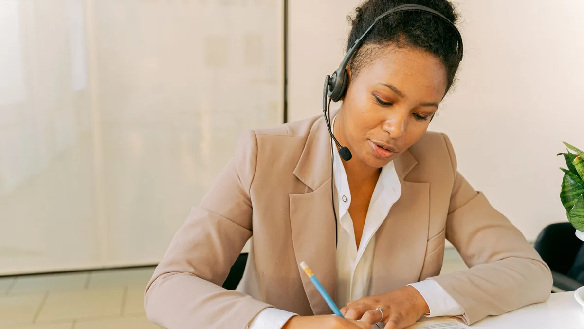 Focused office worker using headset and taking notes in