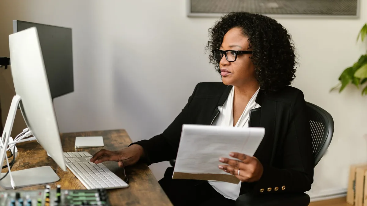 Focused woman working on computer holding documents and