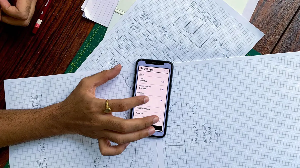 Kâğıttaki uygulama eskizleri üzerinde telefon tutan el