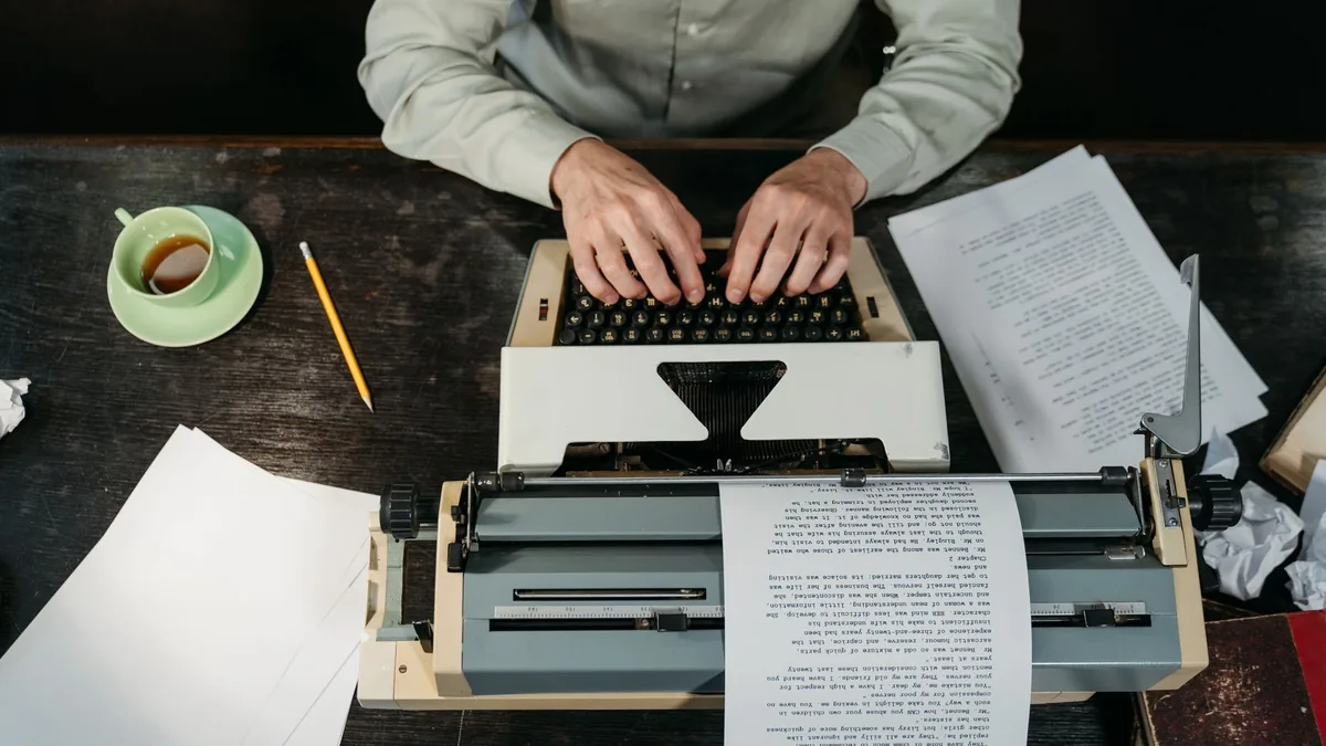 Hands typing on a vintage typewriter with papers and a c