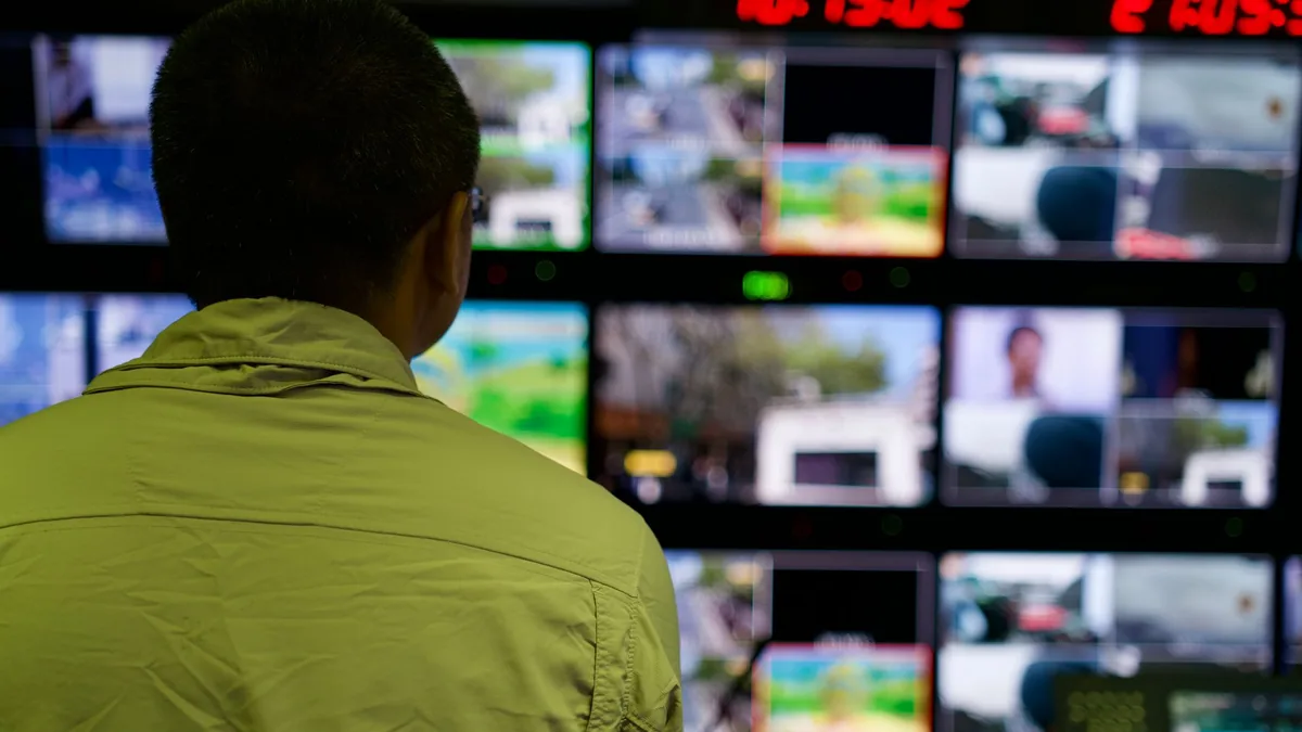 Man in a control room overseeing multiple monitors displ