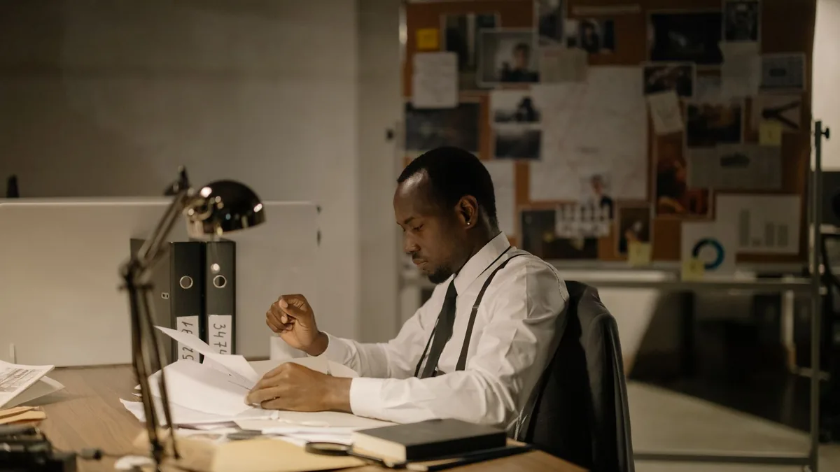 Man in office reviewing documents under desk lamp late h