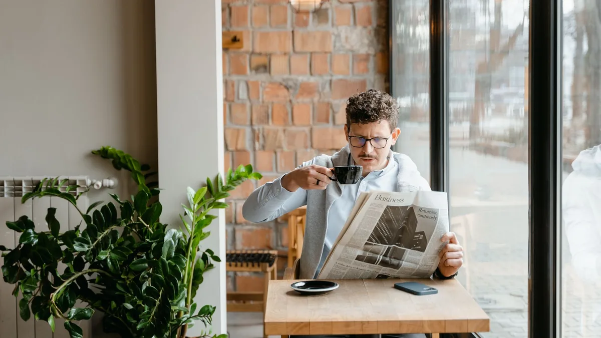 Man sitting indoors with coffee and newspaper surrounded