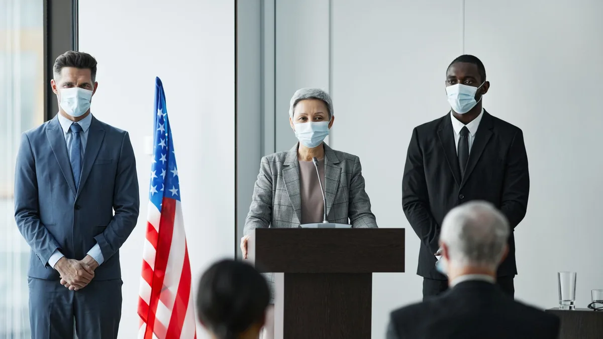 Masked business leaders at a conference podium with us f