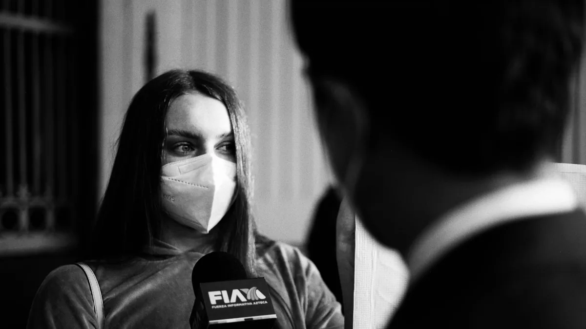 Monochrome image of a masked woman being interviewed hig