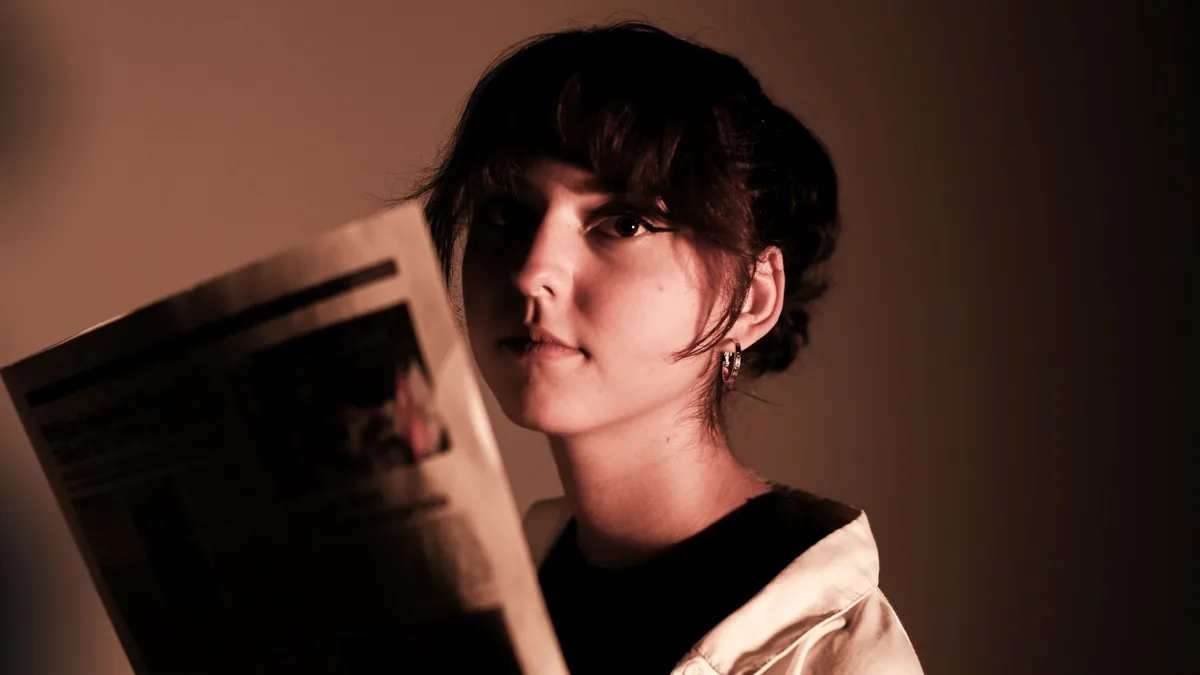 Moody portrait of a young woman holding a newspaper in s