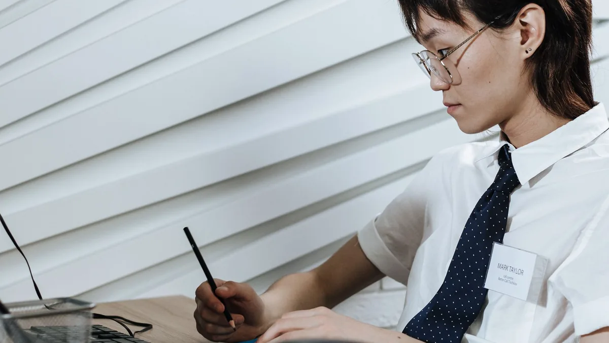 Office worker in eyeglasses taking notes at desk with co