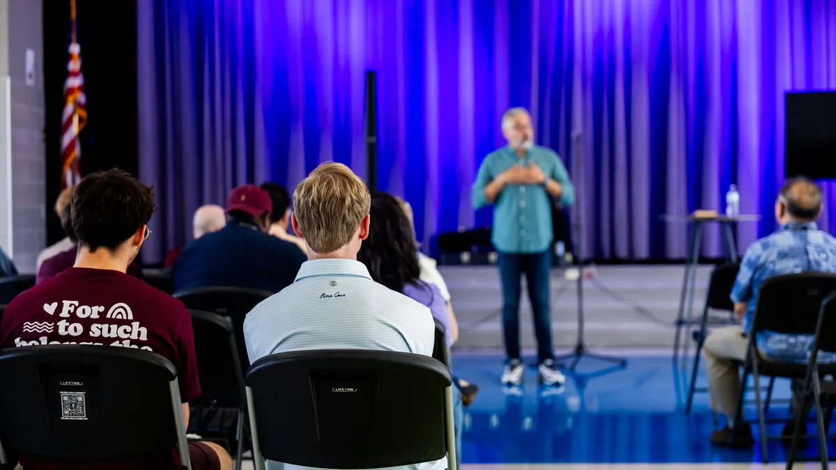 People listening to a speaker in a hall with blue lighti