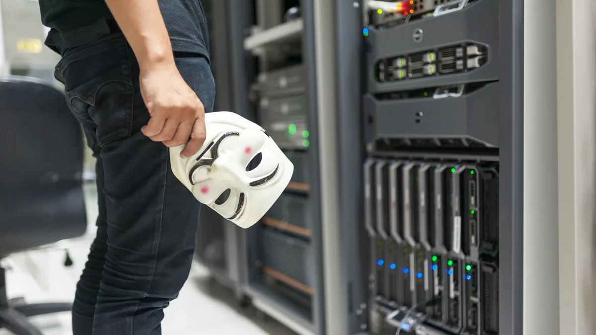 Person holding anonymous mask near servers hinting at cy