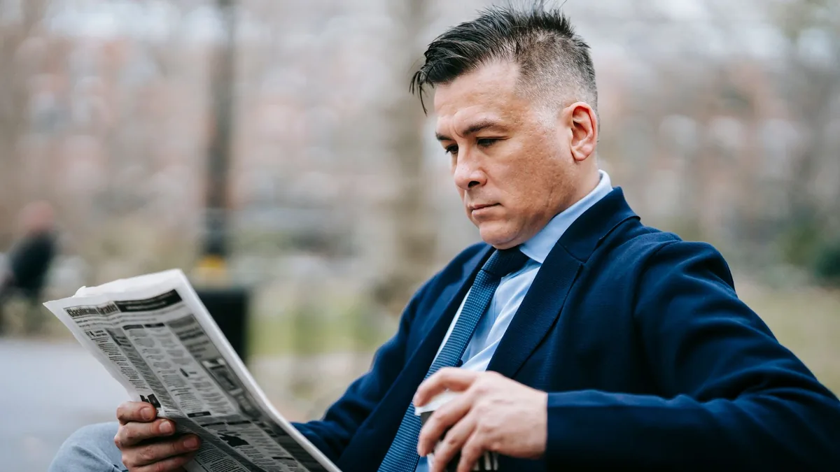Professionally dressed man reading a newspaper on a park