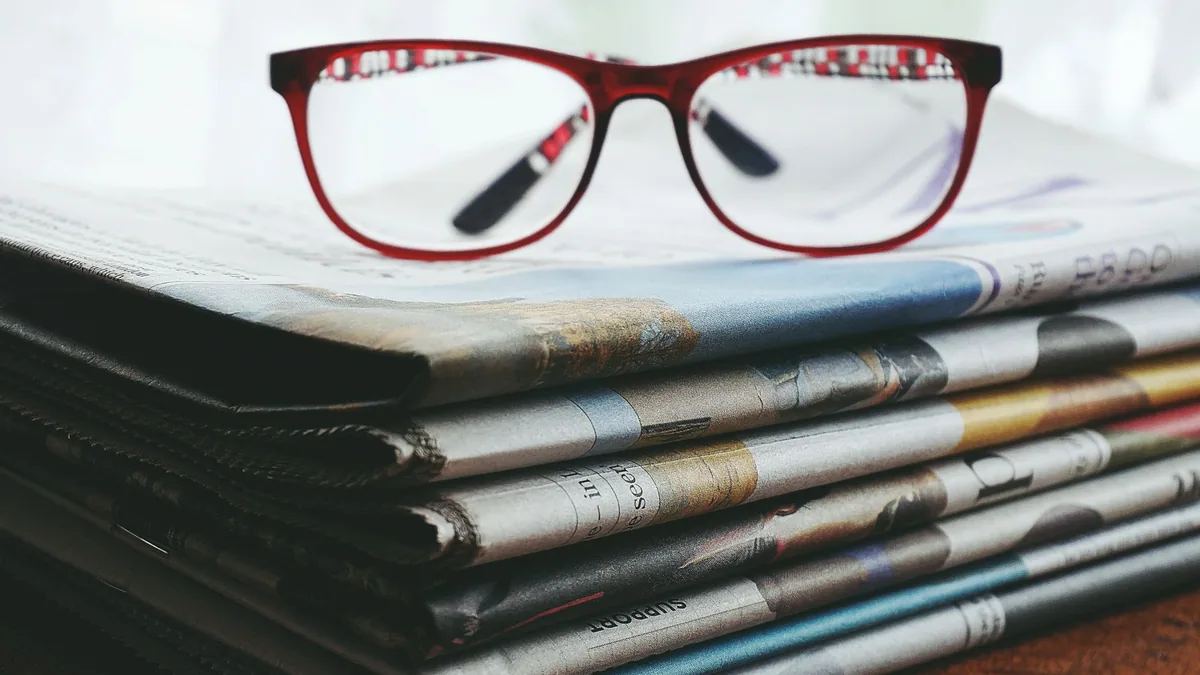 Red eyeglasses resting on a stack of newspapers symboliz