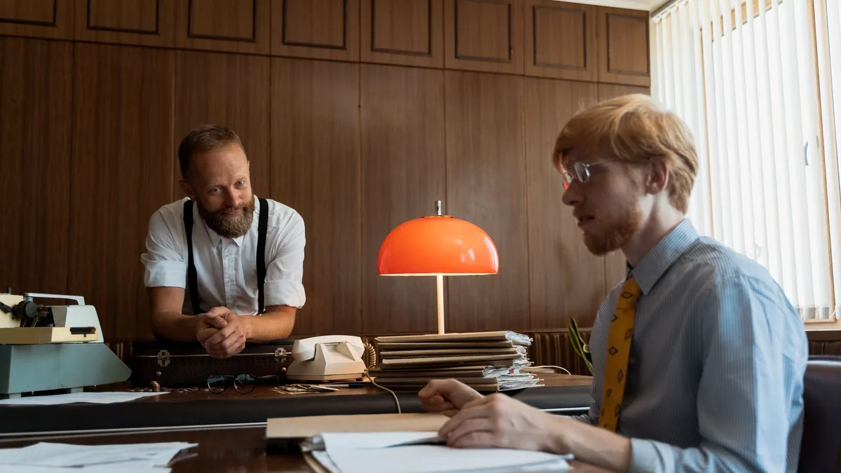 Retro office scene with two men discussing work at a des