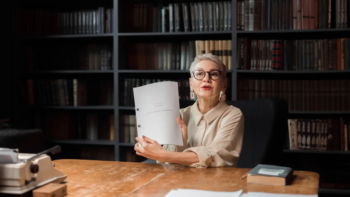 Senior woman with manuscript at a wooden desk in a libra