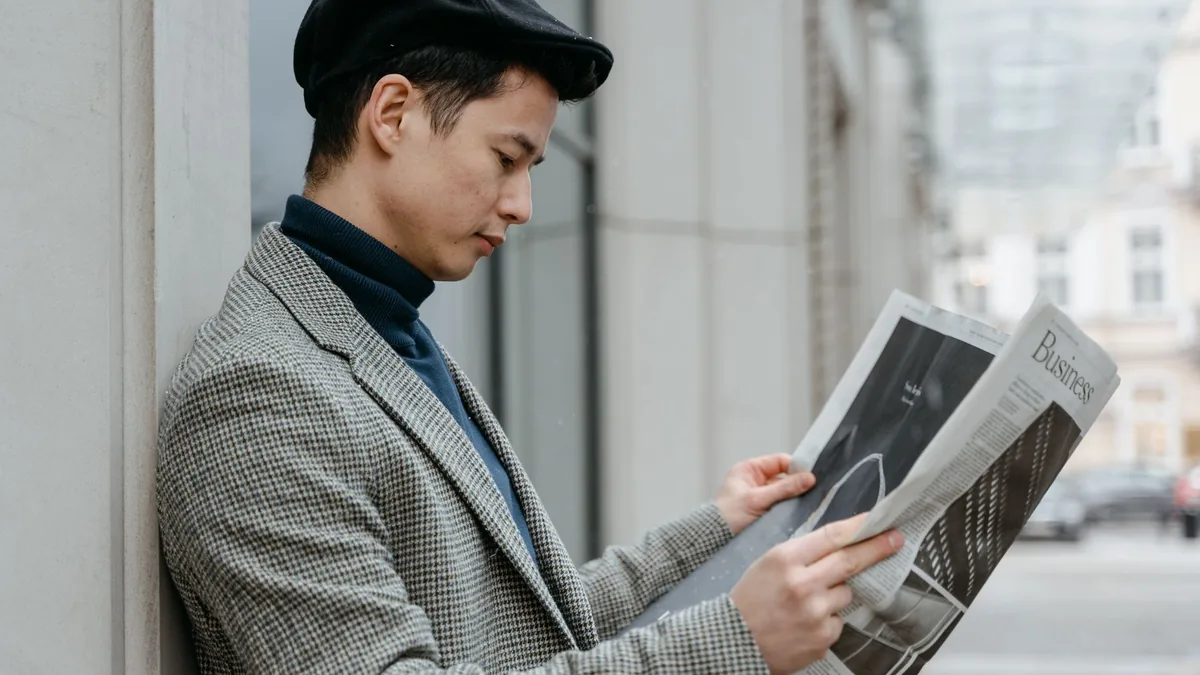 Side profile of a man reading a newspaper outdoors in an