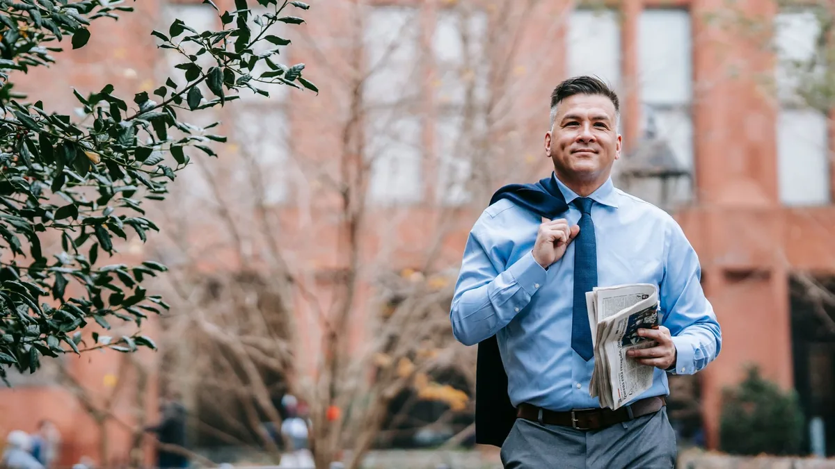 Smiling businessman in formal attire walks outdoors hold