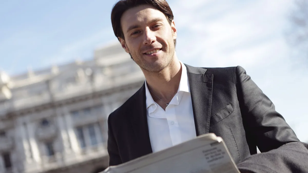 Smiling businessman in suit reads newspaper outside on a