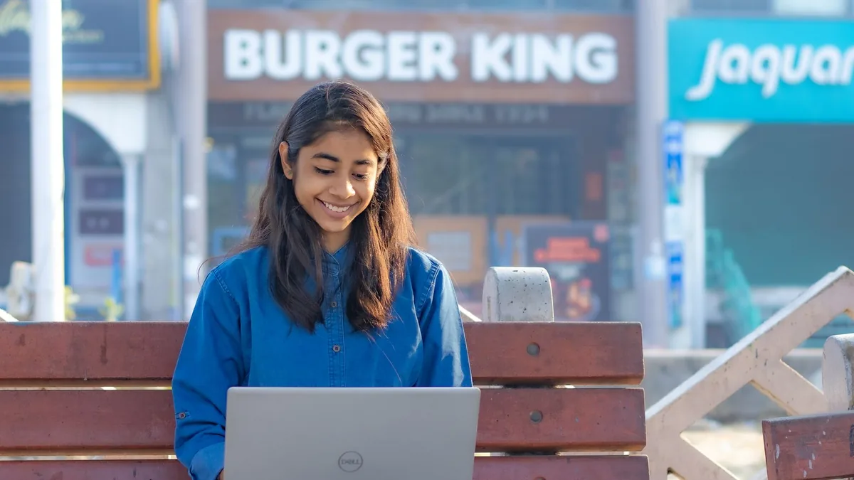 Smiling woman using a laptop on a bench in an outdoor se