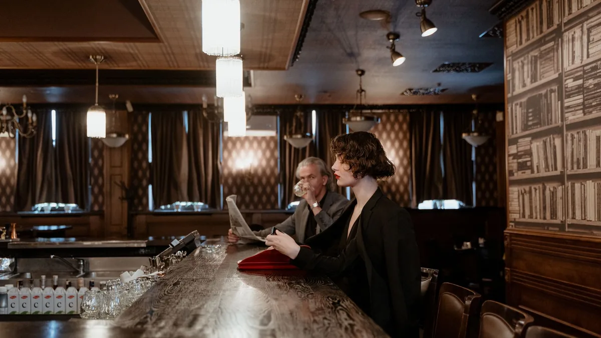 Stylish individuals at a dimly lit bar reading and drink