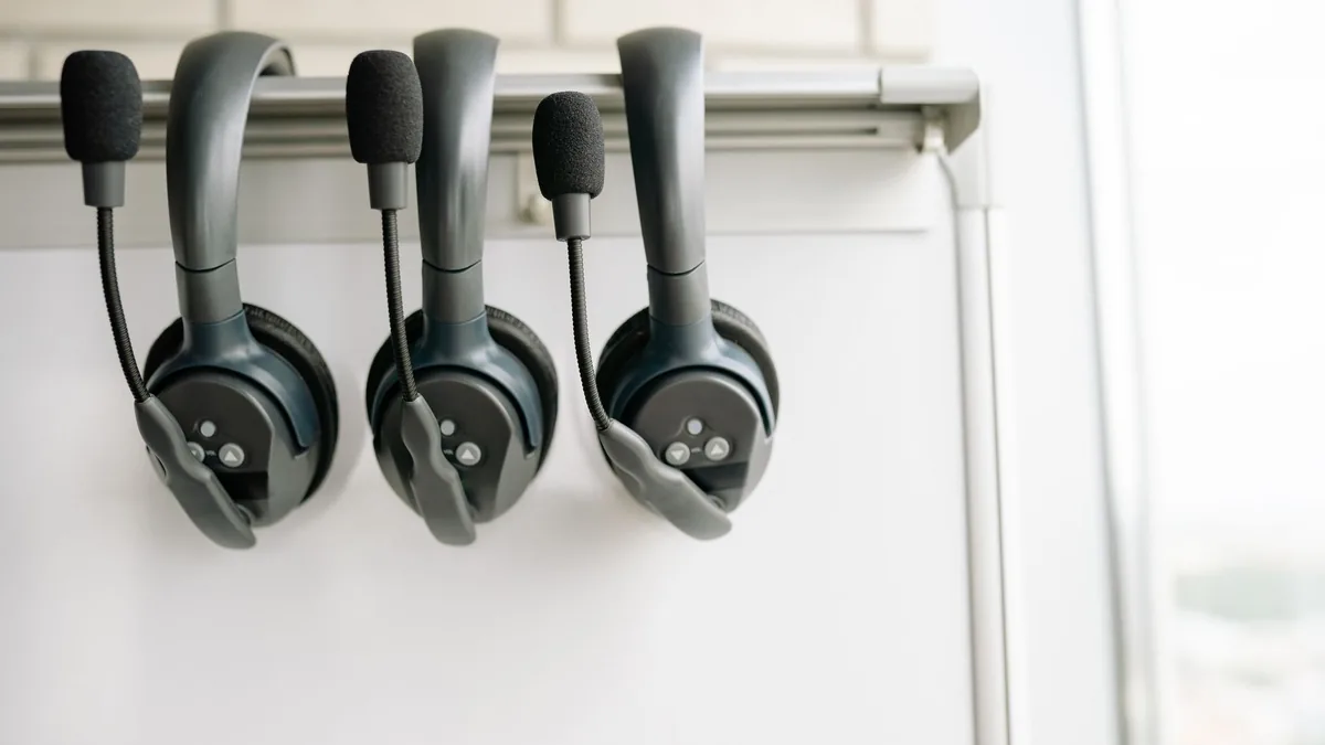 Three black headsets neatly organized on a whiteboard ho