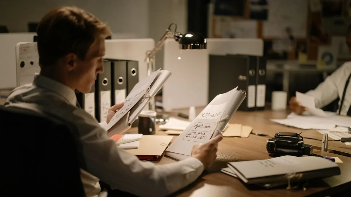 Two detectives reviewing documents in a dimly lit office