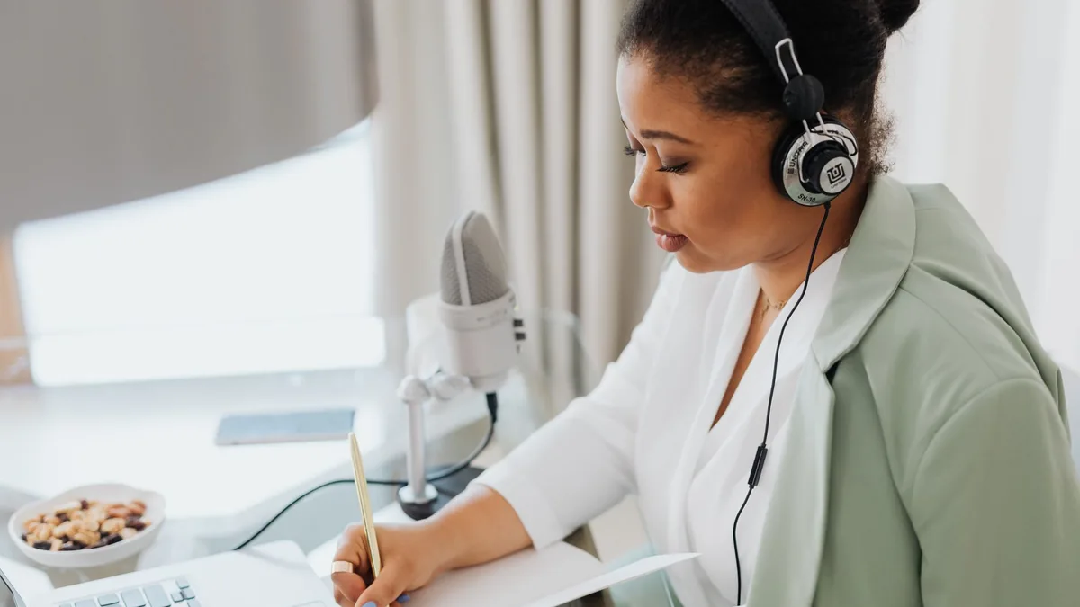 Woman wearing headphones writing notes and working on a